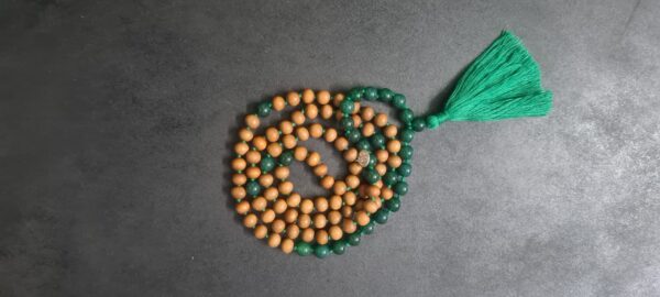 A Green Onyx and Sandalwood Mala Necklace made up of alternating wooden and green beads, with a green tassel at one end, lays coiled on a dark surface.