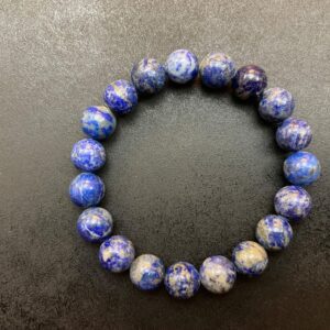 A Blue "Sky" Lapis Lazuli Bracelet made of round, blue and white speckled beads arranged in a circle on a dark background.