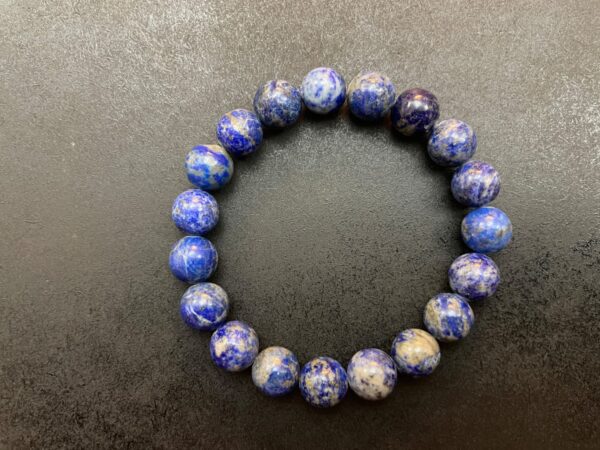 A Blue "Sky" Lapis Lazuli Bracelet made of round, blue and white speckled beads arranged in a circle on a dark background.