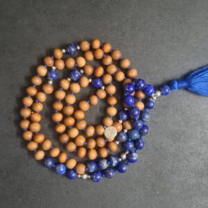 A Blue "Sky" Lapis Lazuli and Sandalwood Mala Necklace with a blue tassel is coiled on a dark surface.