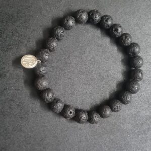 A Grounding Lava Rock Bracelet with a small round metal charm on a dark surface.