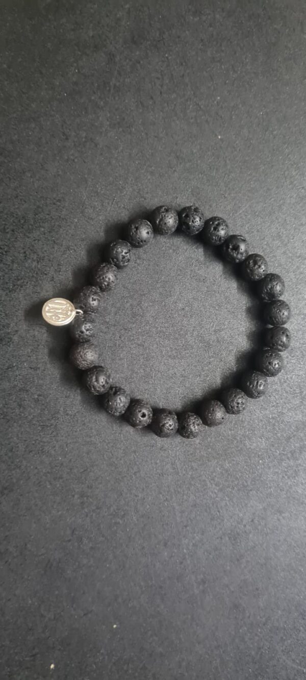 A Grounding Lava Rock Bracelet with a small round metal charm on a dark surface.