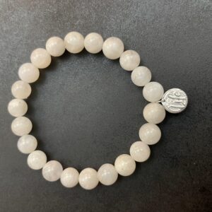 A Moonstone Bracelet made of white stones with a small silver charm, displayed on a dark background.