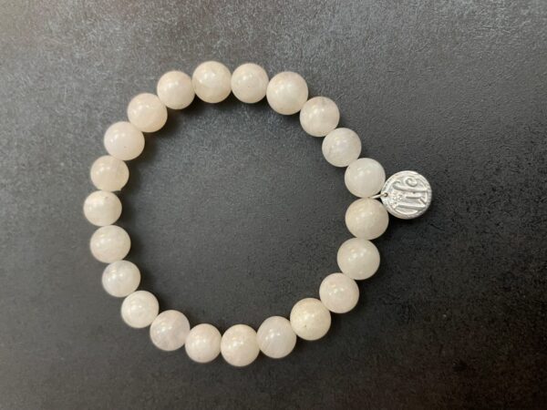 A Moonstone Bracelet made of white stones with a small silver charm, displayed on a dark background.