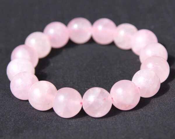 A Rose Quartz Bracelet is arranged in a circular shape on a black background.