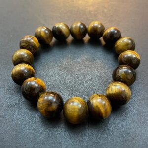 A bracelet made of polished, round Eye of the Tiger Bracelet beads arranged in a circular pattern on a dark surface.