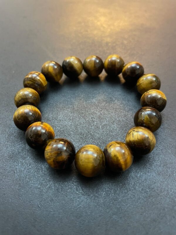 A bracelet made of polished, round Eye of the Tiger Bracelet beads arranged in a circular pattern on a dark surface.