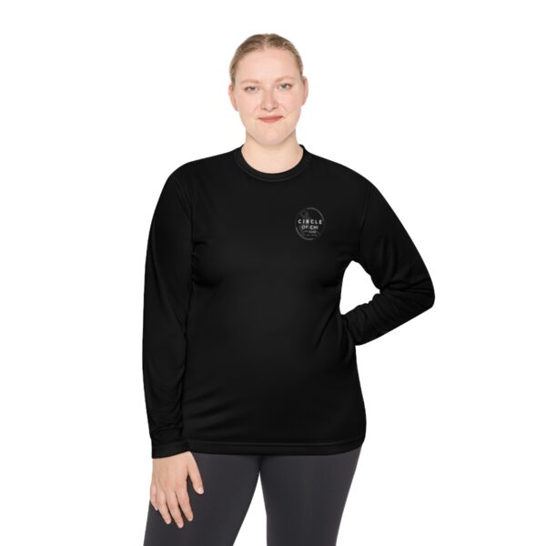 A woman stands against a white background, wearing a Unisex Lightweight Long Sleeve Tee with a small logo on the upper left side and dark leggings.