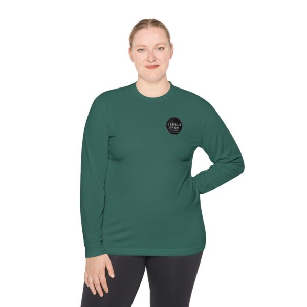 A person with blonde hair in a ponytail is wearing a green, Unisex Lightweight Long Sleeve Tee with black leggings, standing against a plain white background.