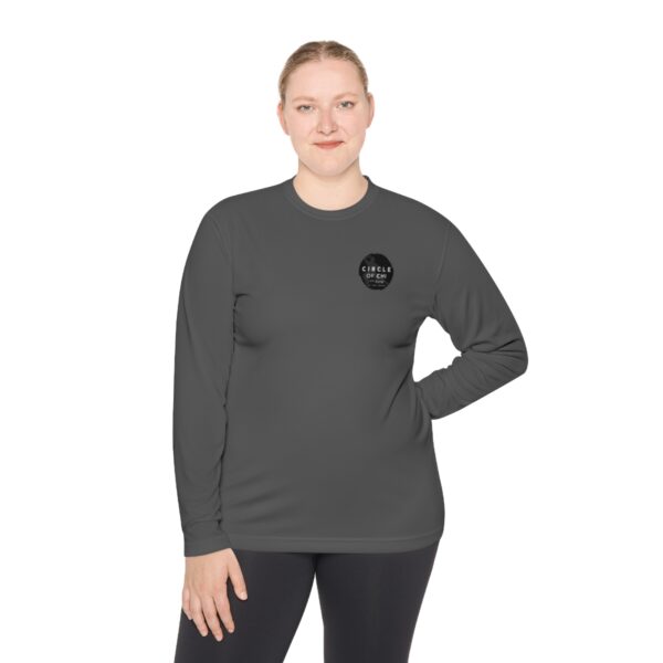 A person is standing with one hand on their hip, wearing an Unisex Lightweight Long Sleeve Tee and black leggings, looking at the camera.