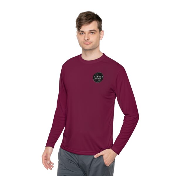 A man in a maroon Unisex Lightweight Long Sleeve Tee and gray pants is standing and facing forward. The shirt has a small black circular logo on the left chest area with the text "Circle of care.