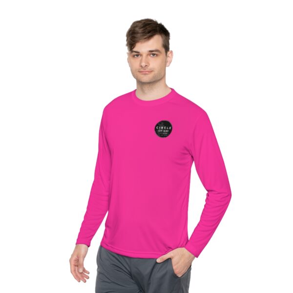 A person wearing a bright pink Unisex Lightweight Long Sleeve Tee with a small black circular logo on the chest that says "Circle of Calm," and gray pants.