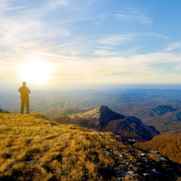 A person stands on a grassy cliff overlooking a vast landscape of hills and valleys at sunrise, listening to Music for Spiritual Transformation Vol. 23 No. 1.