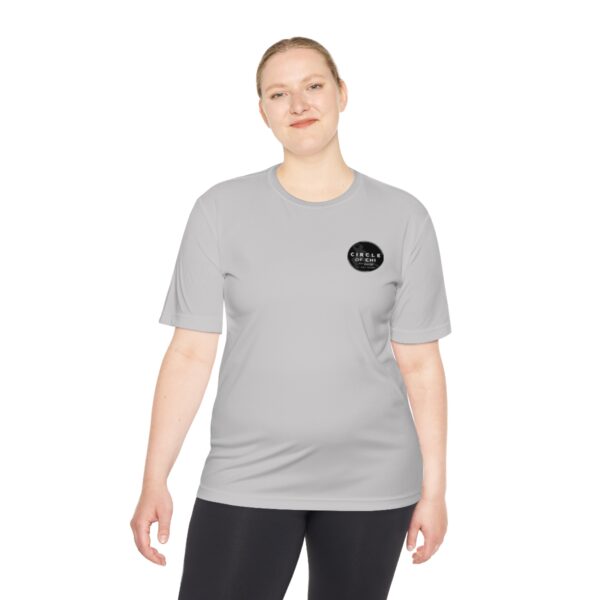 A person with light skin and short hair wearing a Circle of Chi Athletic Tee and black pants stands against a white background.