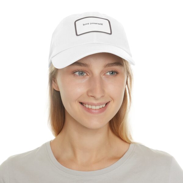 A person wearing a white "Love Yourself Dad Hat" and a light grey shirt, smiling.