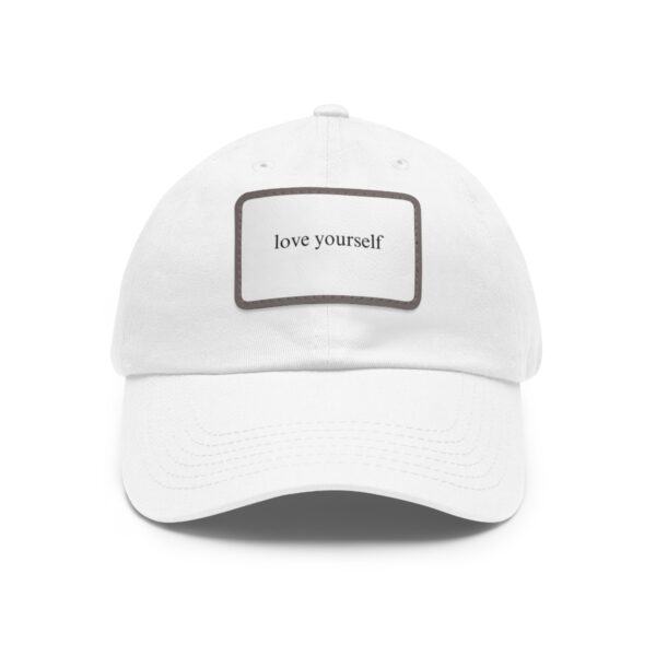 A white Love Yourself Dad Hat with a rectangular patch on the front displaying the words "love yourself" in small, black text.