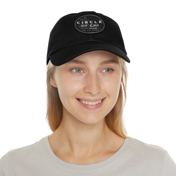 A person with long blonde hair smiles while wearing a Circle of Chi Dad Hat with Leather Patch.