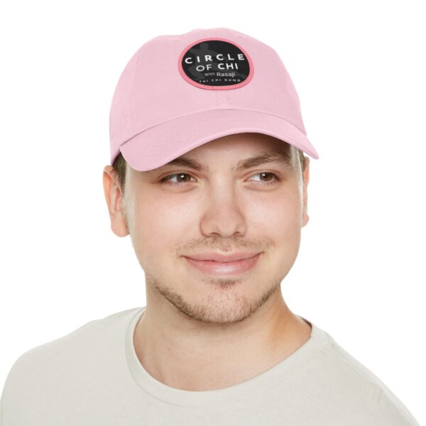 A person wearing a light pink Circle of Chi Dad Hat with Leather Patch. The person is smiling and wearing a light-colored shirt against a white background.